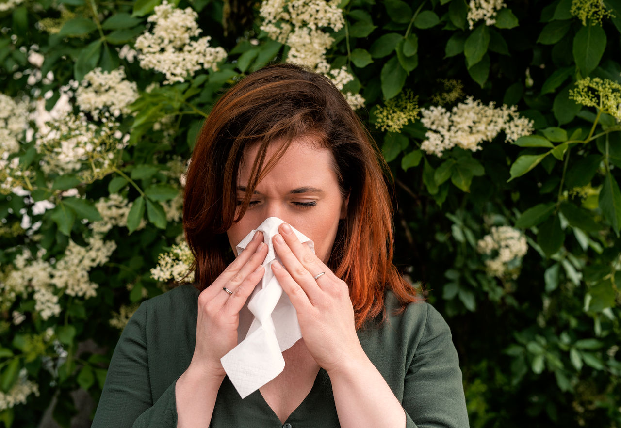 A woman blows her nose while standing in front of flowers